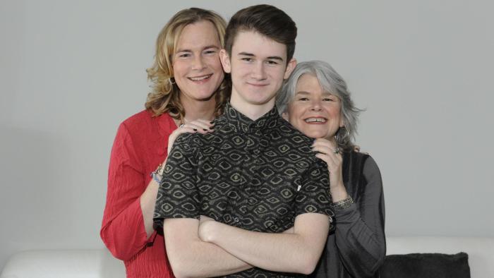 Becoming Us: Family photo with Ben standing in front of two adults, his arms crossed
