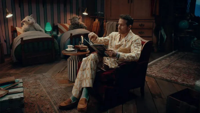 Bedtime Stories With Ryan TV show screenshot 3: Ryan Reynolds sits in his PJs reading a book to two sheep who lay in beds in the background.