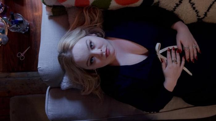 Big Mood TV show screenshot 1: Overhead shot of Maggie, dressed in a low-cut black dress, laying back on her couch with hands clasped across her torso