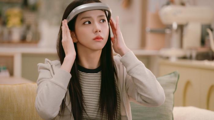 Boyfriend on Demand TV show screenshot 1: Kim Jisoo puts on a silver VR headset. She wears a beige and black striped shirt and a beige hoodie.