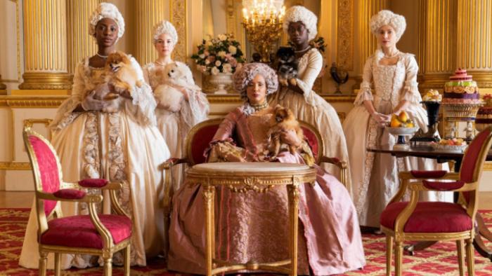 Bridgerton Season 1 TV show screenshot 3: Queen Charlotte is at the center of this show, dressed in a pink gown; four ladies in waiting flank her
