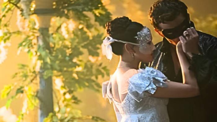 Bridgerton Season 4 TV show screenshot 3: Sophie and Benedict embrace while wearing masks in front of glowing yellow flowers