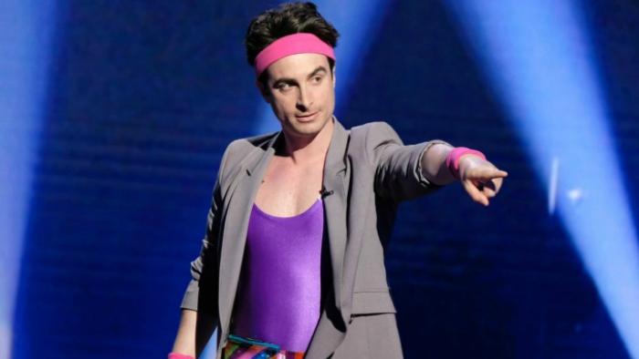 Bring the Funny TV Series: A contestant in pink sweat- and headbands and a purple leotard points at the audience. 
