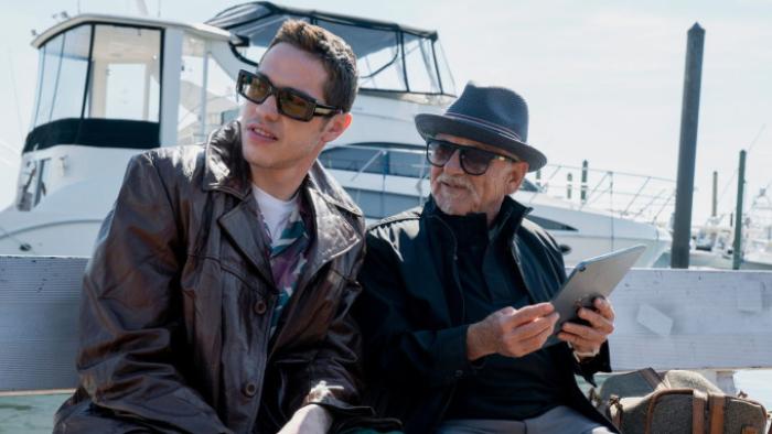 Bupkis TV show screenshot: Joe and Pete sit together in front of a large yacht; both wear sunglasses and black clothing and are looking at something off-camera