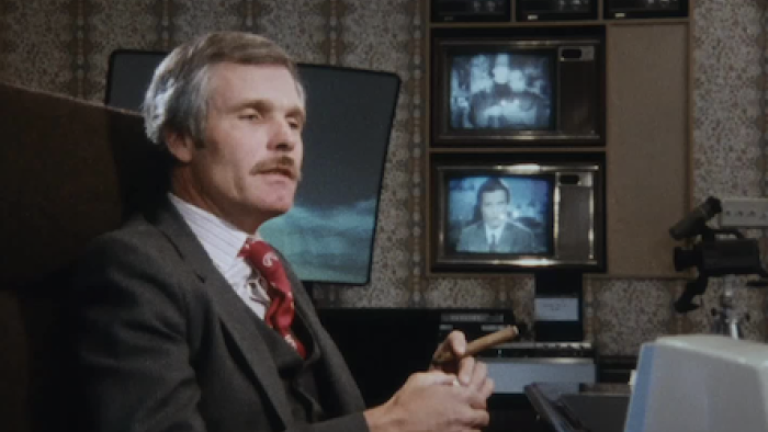  Call Me Ted TV show screenshot 2: Ted Turner sits holding a cigar in room with multiple t.v. sets on wall.