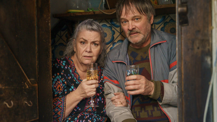 Can You Keep a Secret? TV show screenshot: An older couple peers out a window together holding drinks.