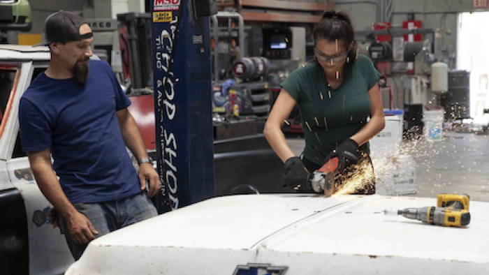 Car Masters: Rust to Riches screenshot 2: Tony Quinones watches Constance Nunes use welding tools on white rusty car hood.
