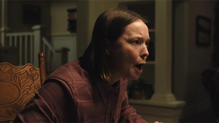 Carrie's mother Margaret is shown sitting in a dimly lit room, appearing upset and animated.