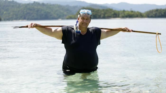 Castaways TV Series: A man stands waist-deep in water, wearing goggles and holding a fishing pole. 