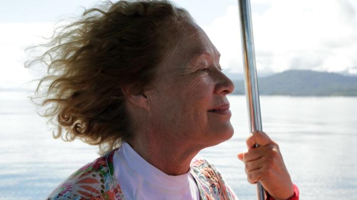Castaways TV Series: A woman leans on a silver metal pole as she looks out over the ocean. 