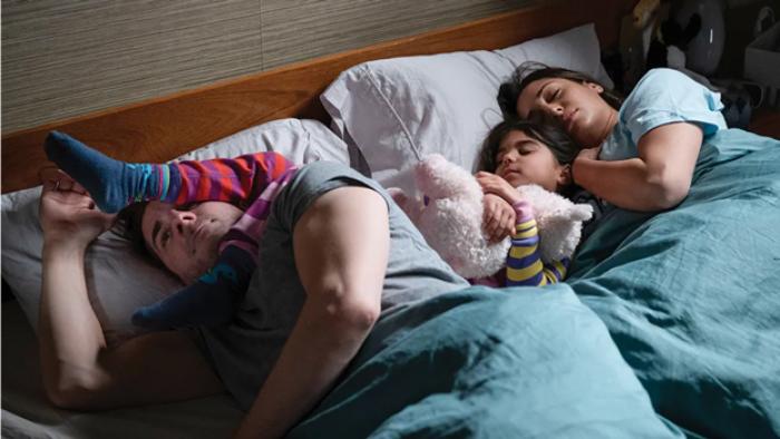 Children Ruin Everything TV show screenshot: a mother and father lay in bed while their two children lay strewn across their heads.