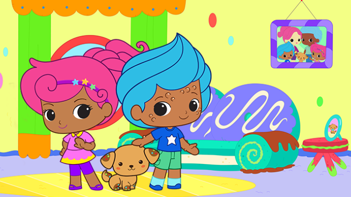 Two animated kids with light brown skin and brightly colored pink and blue hair stand with a dog between them inside a room with a sofa and photograph on the wall