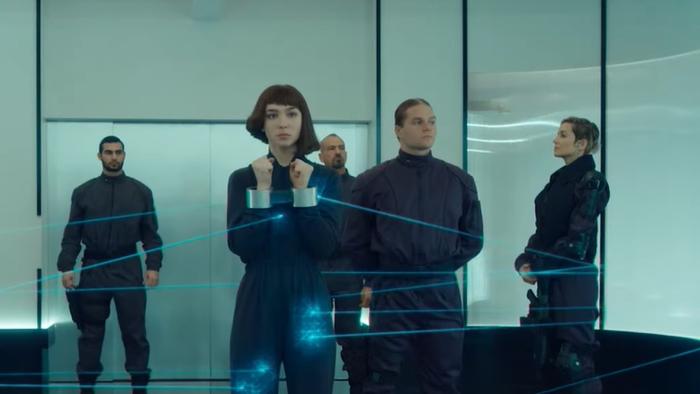 Matilda De Angelis holds her handcuffed wrists up. She is surrounded by guards. Angelis wears a dark blue jumpsuit.