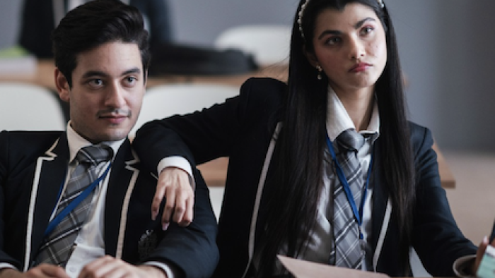 Class TV show: Veers and Yashika sit together smirking in the classroom. 