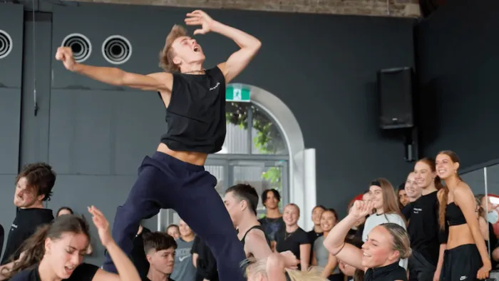 Dance Life screenshot 3: One male dancer with head thrown back and arms akimbo dances above a full studio of dancers