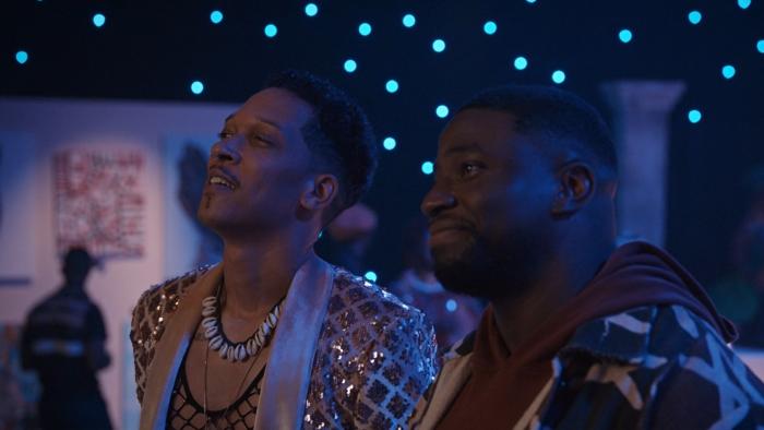 Demascus TV show screenshot 2: Caleb Eberhardt and Okieriete Onaodowan stand in art gallery. Eberhardt wears a fishnet top and a sequin blazer.