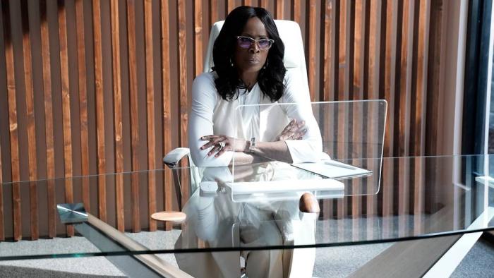 Demascus TV show screenshot 3: Janet Hubert sits at a glass desk in front of a holographic screen. She wears a cream pantsuit and a white top.