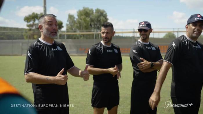 Destination: European Nights TV show screenshot 1: Four men in soccer uniforms stand on a field talking.