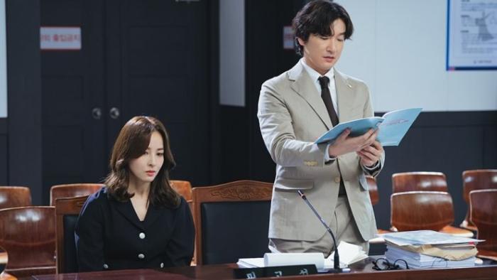 Hye-jin Han and Cho Seung-woo inside a courtroom. Hye-jin Han sits while Cho Seung-woo stands.