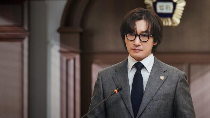 Cho Seung-woo speaking into a microphone while inside a courtroom.