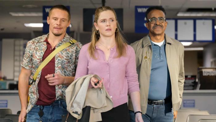 DMV TV show screenshot 1: (L-R) Tony Cavalero, Harriet Dyer, and Tim Meadows walk down a corridor of chairs. They carry bags and jackets.