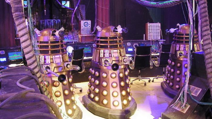 Doctor Who TV Show: Three robotic machines in a metallic room, purple lighting