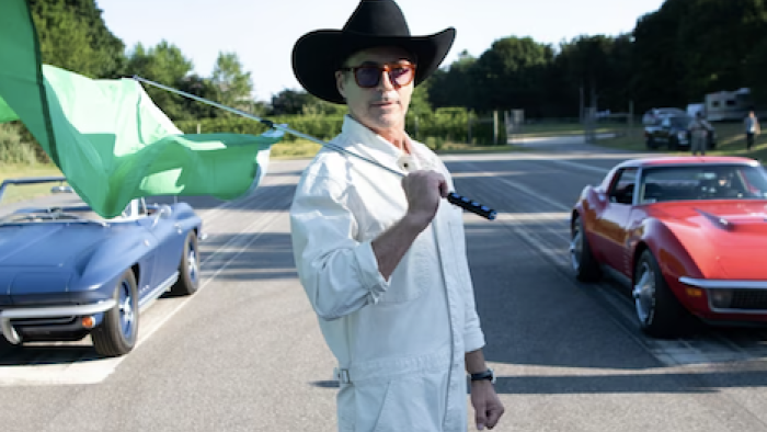 Downey's Dream Cars screenshot 1: Robert Downey Jr. in cowboy hat and white outfit holding flag in front of blue and red classic cars.