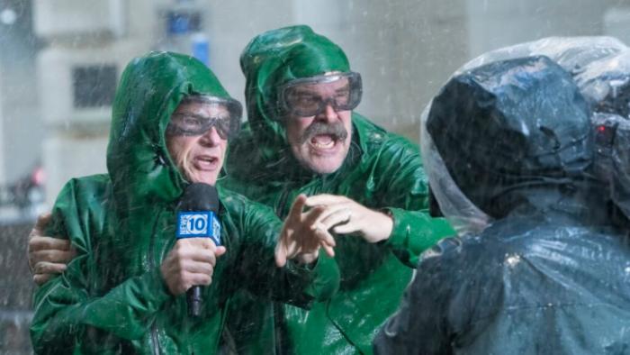 DTF St. Louis TV show screenshot 2: Clark and Floyd wear green rain slickers and Clark holds a microphone as they report from a fierce storm
