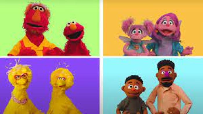 Elmo, Big Bird, Abby Cadabby, and Wes stand in brightly colored squares with their parents. 