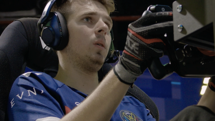 Esports World Cup: Level Up TV show screenshot 1: A male gamer with earphones sits in driver's chair of racing game.