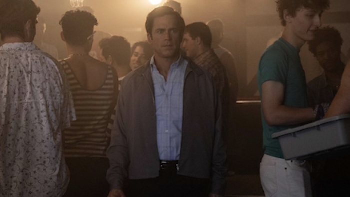 Fellow Travelers TV show screenshot 4: An older Hawks stares forward surrounded by LGBT+ men in bar. 