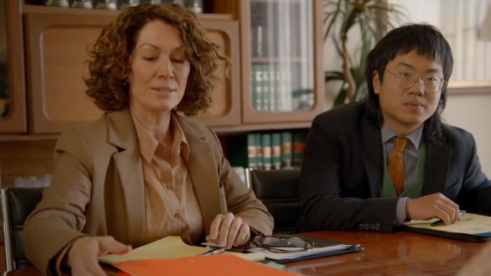 Fisk TV show screenshot 2: Kitty Flanagan and Aaron Chen talk over paperwork and legal pads.