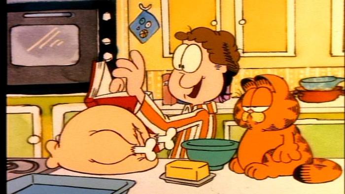 Garfield's Thanksgiving TV: In the kitchen, Jon excitedly reads the from his recipe book while Garfield stares blankly at the Thanksgiving turkey.