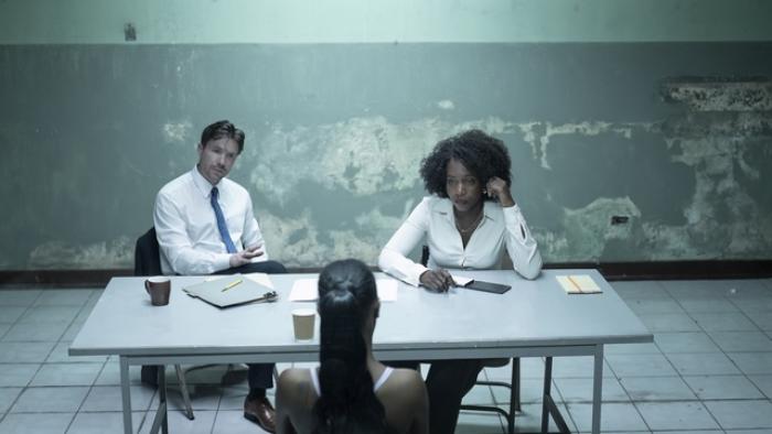 Joe Dempsie and Tamara Lawrence interrogate Shernet Swearine at a table. Files are strewn across the table.