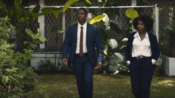 Gershwyn Eustache Jnr and Tamara Lawrence walk on the grass outside. They are both dressed in office business clothes.
