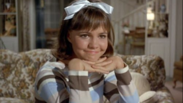 Gidget screenshot 1: Gidget with a white bow, smiling, seated in a cozy living room.