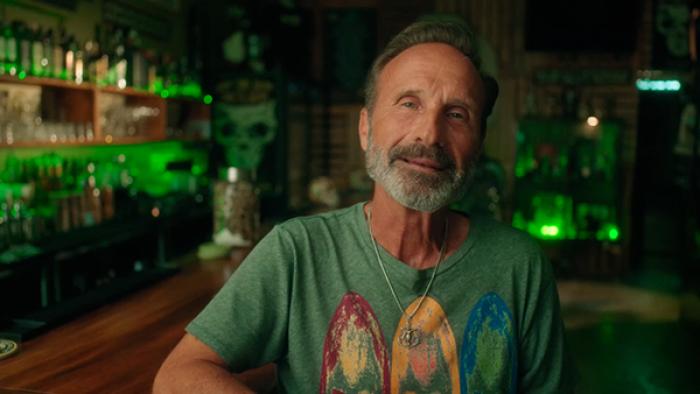 Glitter and Greed: The Lisa Frank Story TV show screenshot 1: James Green wears a green t-shirt and sits at a bar, facing the camera.