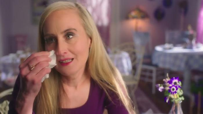 Glitter and Greed: The Lisa Frank Story TV show screenshot 2: A former employee with long, blonde hair and a purple shirt dabs her eyes with a tissue.