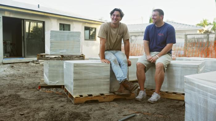 Going Home with Tyler Cameron: Tyler Cameron and his construction business partner sit on materials in a yard.