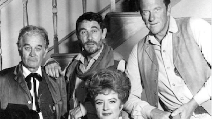 Gunsmoke screenshot 1: Doc Adams, Chester Goode, Kitty Russell, and Matt Dillon lean against stairs.