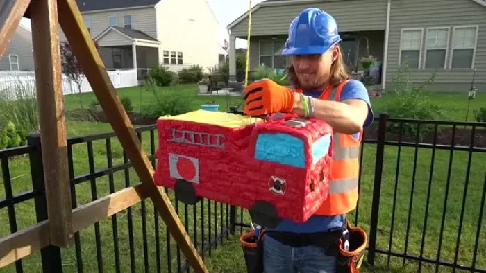 Handyman Hal TV: Handyman Hal holding a red firetruck piñata outside.