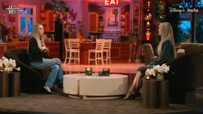 Hannah Montana 20th Anniversary Special screenshot 1: Alex Cooper interviews Miley Cyrus in front of the living room set of Hannah Montana's house.