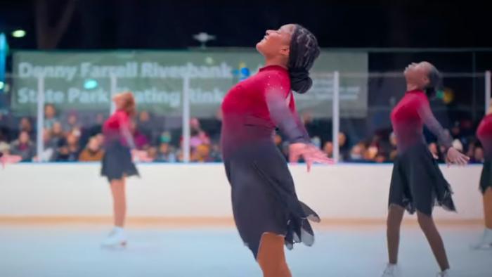 Harlem Ice TV show screenshot 1: Adrianna poses with arms back, chin high and a large smile in the middle of a figure skating presentation. 