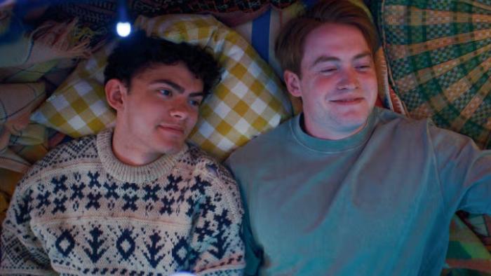 Heartstopper Forever TV show screenshot 2: Charlie and Nick lie together on a bed, fully clothed; each is looking up and smiling together