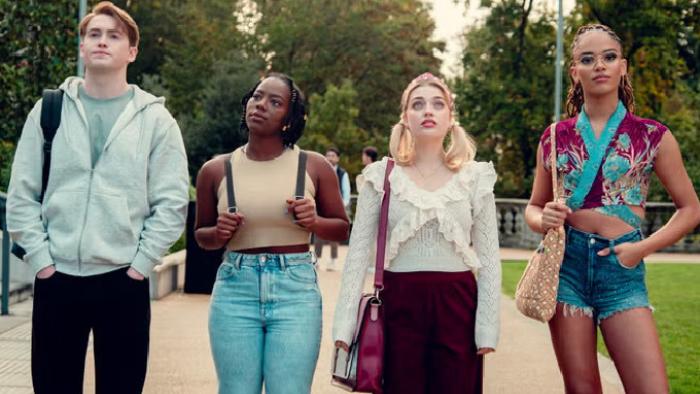 Heartstopper Forever TV show screenshot 3: Nick, Tara, Imogen and Elle, dressed casually, stand lined up across a road, staring at the distance