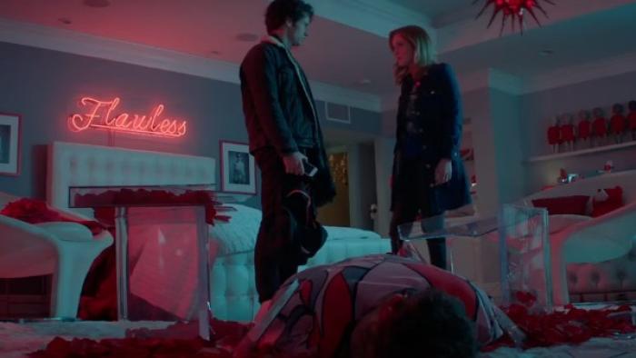 Heathers TV Series: A male and female teen stand over a girl lying on the floor of her bedroom; behind them, a neon sign reads "Flawless." 