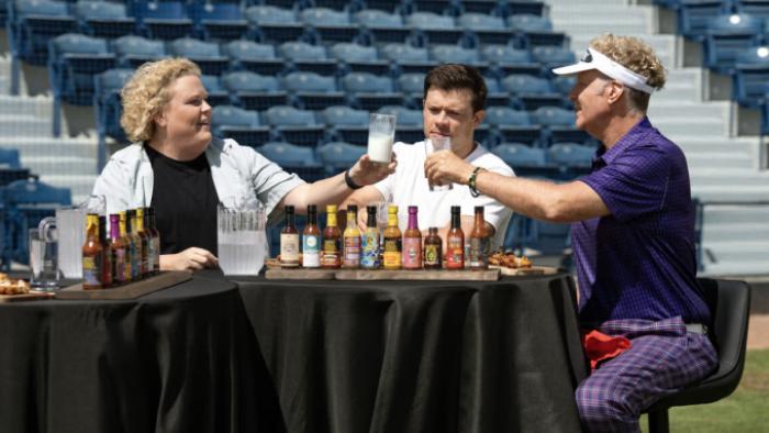 Hot Ones: Extra Heat TV show screenshot 1: Fortune Feimster and Will Ferrell clink glasses of milk as they prepare to eat hot wings