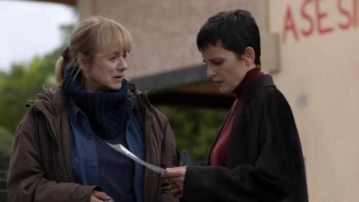 Emma Suárez and Elena Anaya. Suárez wears a blue sweater and brown coat. Anaya wears a red sweater and a dark coat.