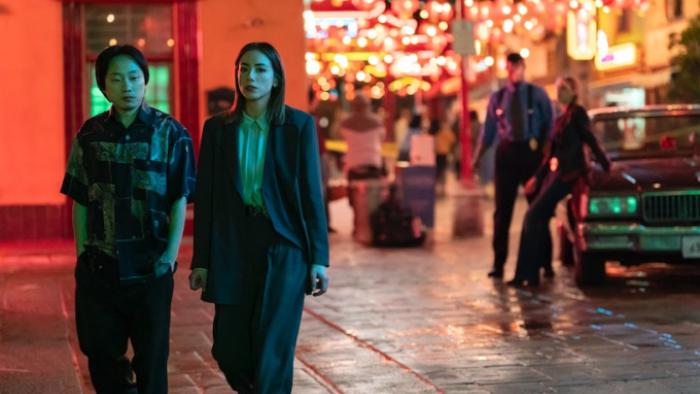 Interior Chinatown TV show screenshot 2: Willis and Lana walk together down a Chinatown street, glowing with a red light; behind them is a man staring