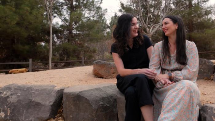 It's OK to Ask Questions: Two women smile and cuddle as they are interviewed in a forest setting